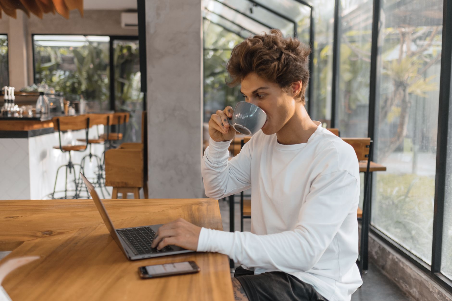 Un jeune homme boit un café en tapant sur son ordinateur portable dans un café lumineux